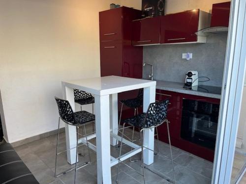 une cuisine avec des placards rouges, une table blanche et des tabourets dans l'établissement Appartement T2 Climatisé au Cœur du Cap d'Agde, proche Port et Plages, 4 Personnes - FR-1-749-41, au Cap d'Agde