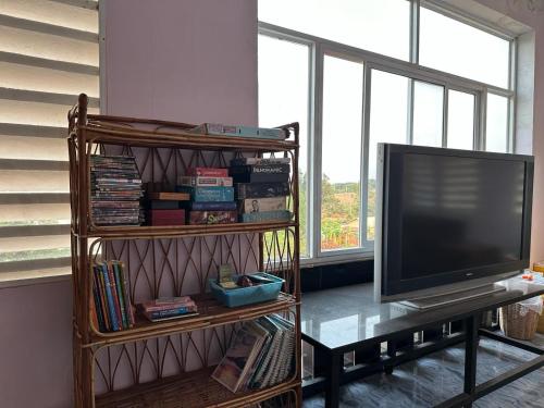 a living room with a tv and a shelf with books at The Vibe Guesthouse in Kampot