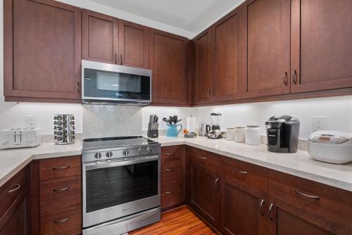 a kitchen with wooden cabinets and a stove and a microwave at @Marbella Lane-Pōmaika'i LoveNest Ocean+MT View in Waianae
