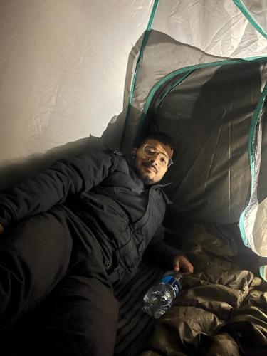 a man laying in a tent with a water bottle at Triund Trek in Dharamshala
