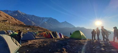 a group of people standing next to tents on a mountain at Triund Trek in Dharamshala