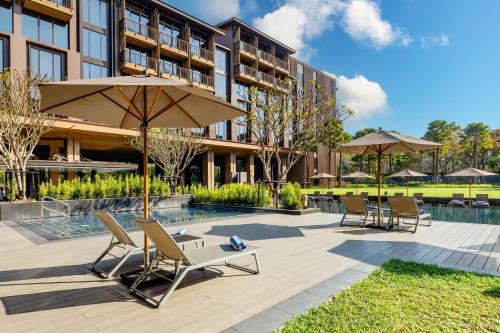 eine Terrasse mit Stühlen, einem Sonnenschirm und einem Pool in der Unterkunft Courtyard by Marriott Bangkok Suvarnabhumi Airport in Bangkok