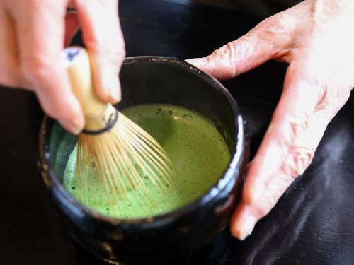a person holding a whisk in a pot of green liquid at Fukeikan 風景館 in Takayama