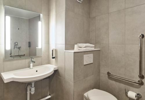 a bathroom with a sink and a toilet and a mirror at B&B HOTEL Versailles Rocquencourt in Rocquencourt