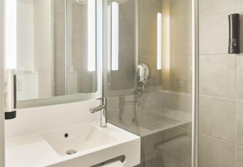 a bathroom with a sink and a shower with a mirror at B&B HOTEL Versailles Rocquencourt in Rocquencourt