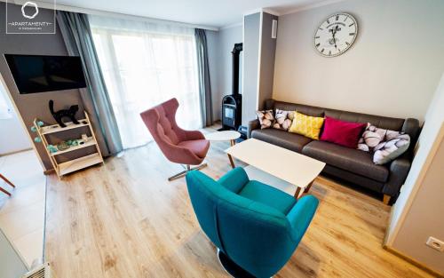 a living room with a couch and chairs and a clock at Wonder Home - Domki górskie na osiedlu dozorowanym, z kominkami i placem zabaw in Karpacz