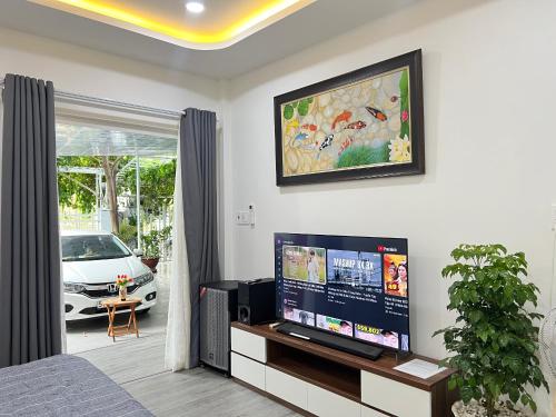 un soggiorno con una TV a schermo piatto su una parete di Green Jungle Homestay - Phù Hợp Gia Đình Từ 10 - 15 Người Lớn & 5 Trẻ Em - Bãi Đậu Xe Ô Tô, Sân BBQ - Miễn Phí Sử Dụng Dịch Vụ Hồ Bơi Cách Homestay 3 Phút Đi Bộ - 7 Phút Đi Bộ Đến Biển - 5 Phút Đến Chợ Hải Sản Phú Thuỷ a Phan Thiet