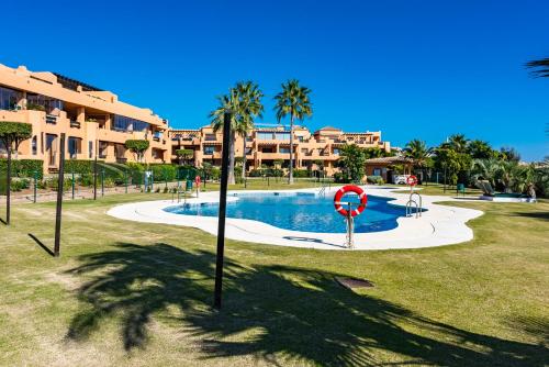 uma piscina num parque com palmeiras e um edifício em Casares Costa Gem: 2BR with Pool em Bahia de Casares