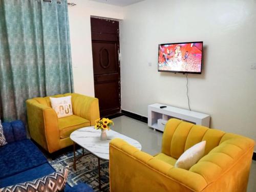 a living room with two yellow chairs and a tv at Mellow Homes 1 & 2 Bedrooms fully furnished Apartment in Kitengela 