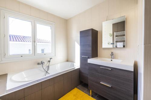 une salle de bain avec une baignoire, un lavabo et un miroir dans l'établissement La maison de Parrain - A proximité des plages, à Saint-Nazaire