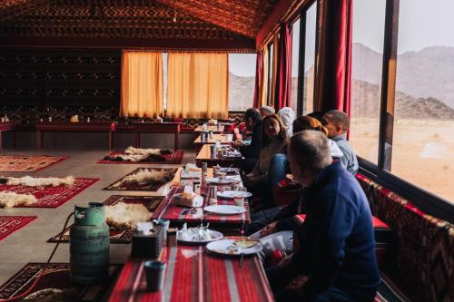 um grupo de pessoas sentadas numa longa mesa com comida em Bedouin Nights Camp em Wadi Rum