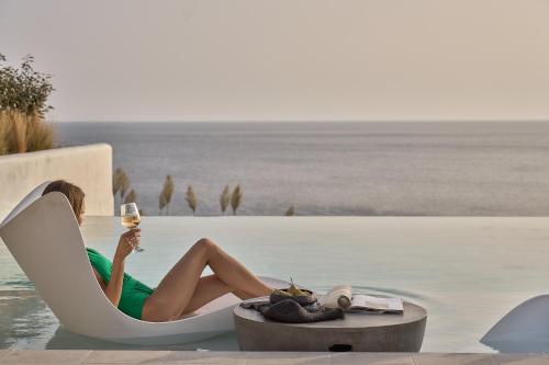 a woman sitting in a chair with a glass of wine at Ios Grand Pool Suites in Mylopotas