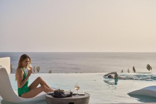 a woman sitting on a chair drinking wine next to a swimming pool at Ios Grand Pool Suites in Mylopotas