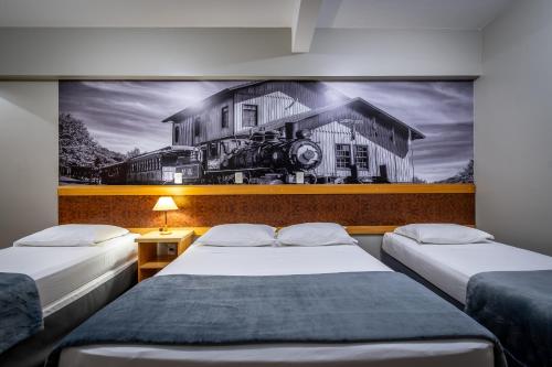 2 camas en una habitación con una pintura de una casa en Brivali Hotel e Eventos en Caçador