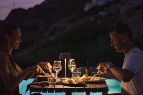 a man and woman sitting at a table with food and wine glasses at Ios Grand Pool Suites in Mylopotas