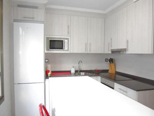 uma cozinha com armários brancos e um frigorífico branco em Sunshine beach Gijón em Gijón