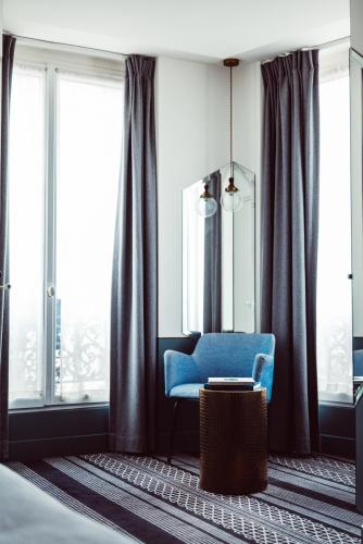 a living room with a blue chair and large windows at Hotel Panache in Paris