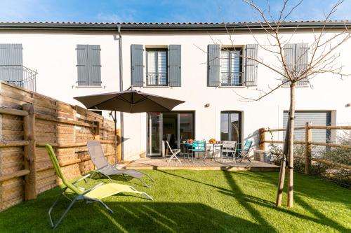 einen Garten mit Sonnenschirm und Stühlen vor einem Haus in der Unterkunft Villa Paulina, cœur village, à 5 min de la plage in Portiragnes