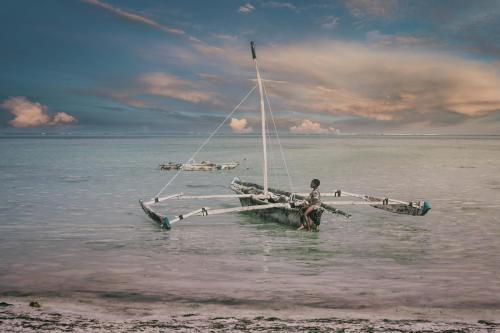 a man standing in the water next to a boat in the ocean at Oxygen Paje Hotel in Paje
