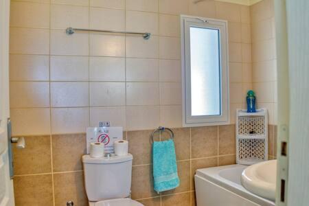 a bathroom with a toilet and a sink and a window at Joya Cyprus Sapphire Garden Apartment in Saint Amvrosios