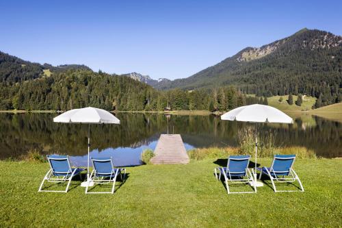 eine Gruppe von Stühlen und Sonnenschirmen neben einem See in der Unterkunft Arabella Alpenhotel am Spitzingsee, a Tribute Portfolio Hotel in Spitzingsee