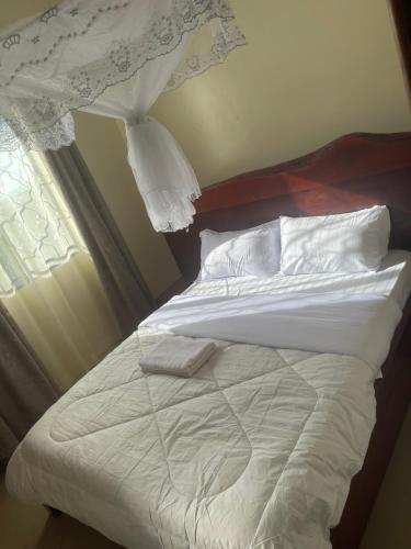 Cama con sábanas blancas y almohadas junto a una ventana en 7 Days Hotel en Entebbe