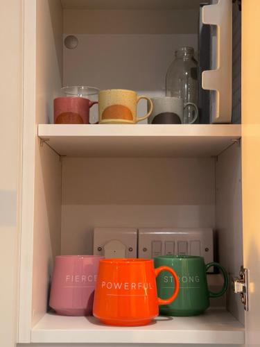 a cupboard filled with colorful coffee mugs at Stylish Brentford Riverside Penthouse in Brentford