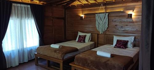 two beds in a room with wooden walls and a window at Jembrana Bali Homestay in Pengambengan