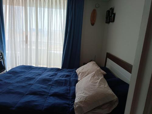 ein Schlafzimmer mit einem Bett mit blauer Decke und einem Fenster in der Unterkunft Departamento Aquamar in Viña del Mar