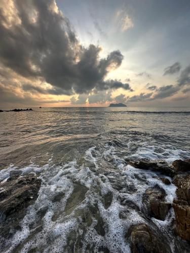 a sunset over the ocean with rocks in the water at The Beach Resort & Residence - SHA Plus in Pathiu