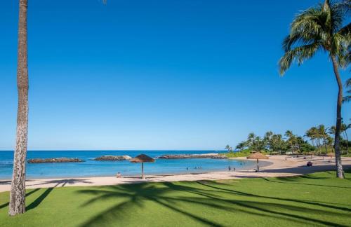 a beach with palm trees and the ocean with people on it at Ko Olina Beach Villas O1111 in Kapolei