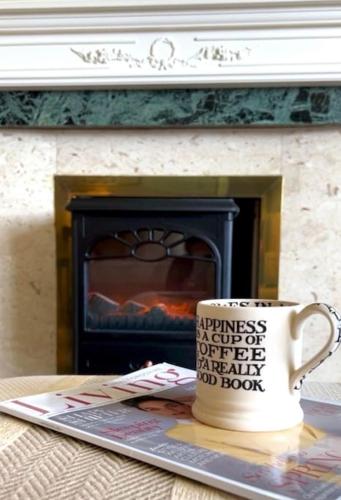 a coffee cup sitting on a table in front of a fireplace at Vast, Elegant Home with Indoor Pool & Sauna near Popular Golf Course in Kington