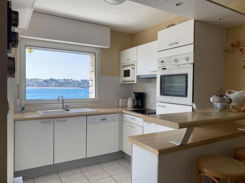 une cuisine avec des placards blancs et une grande fenêtre dans l'établissement 500 - T2 avec balcon vue mer et proche du port, à Erquy
