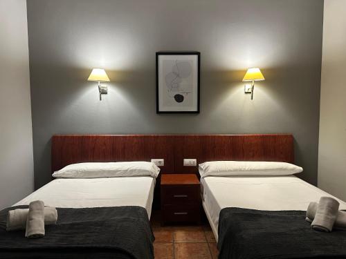 two beds in a room with two lamps on the wall at Hotel La Pardina in Sabiñánigo