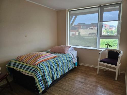 1 dormitorio con 1 cama, 1 silla y 1 ventana en Departamento a minutos del Lago, en Puerto Varas