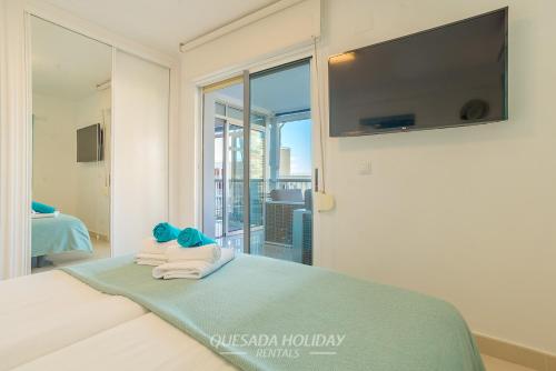 a room with a bed with towels and a flat screen tv at La Perla Benidorm Apartment seaview & pool Levante Beach in Benidorm