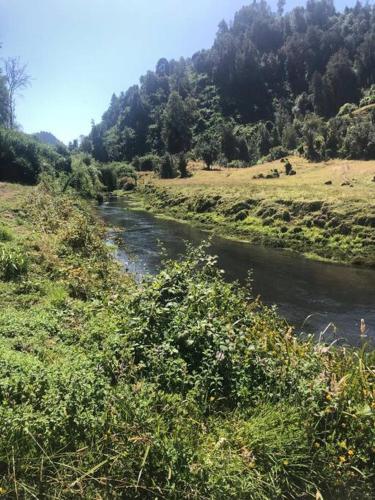 a river in a field next to a hill with trees at Casa campo en plena naturaleza 3 dormitorios y 2 baños in Lago Ranco