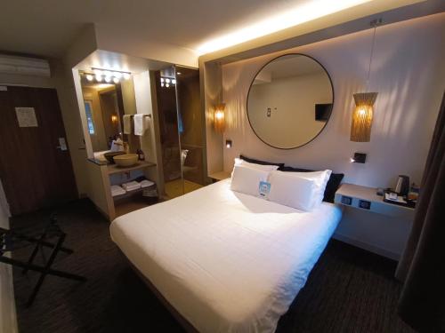 a hotel room with a large bed and a mirror at Hôtel Kyriad Brive Ouest in Brive-la-Gaillarde
