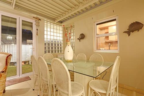 Bayview 30 by HostAgents في بلوبيرجستراند: غرفة طعام مع طاولة زجاجية وكراسي بيضاء