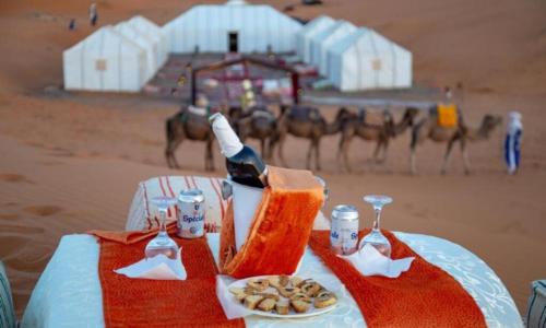 a table with a bottle of wine and a plate of food at Merzouga Luxurious Camp in Merzouga