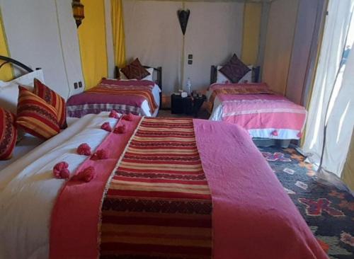 a room with two beds with pink and red blankets at Merzouga Luxurious Camp in Merzouga