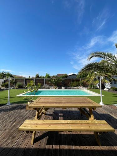 une terrasse en bois avec une table de pique-nique et une piscine dans l'établissement Charmante Maison entre châteaux et océan, à Cussac-Fort-Medoc