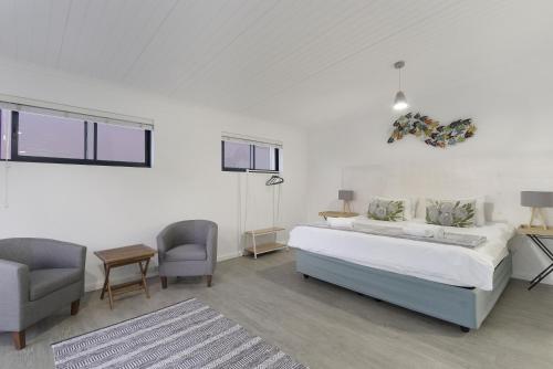 a white bedroom with a bed and a chair at Korhaan House in Melkbosstrand