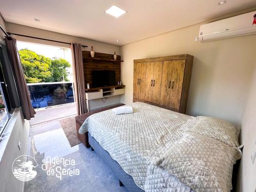 1 dormitorio con 1 cama, TV y ventana en Incrível suíte com vista para a Praia do Viana, en Ilhabela