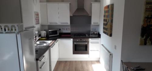 uma cozinha com armários brancos e electrodomésticos de aço inoxidável em Spacious Modern Apartment em Glasgow