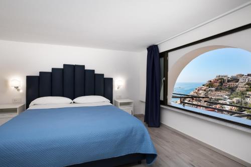 YourHome - H2O Marina Apt Sea View في بوسيتانو: غرفة نوم بسرير ازرق ونافذة كبيرة