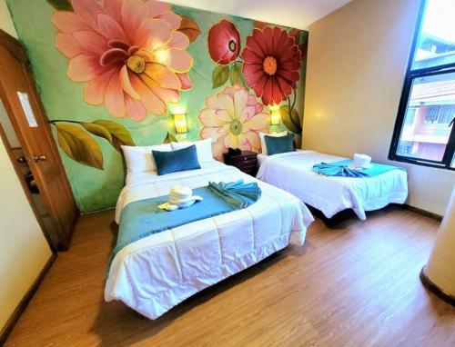 Habitación con 2 camas y flores pintadas en la pared. en Hotel Virgen del Cisne en Loja
