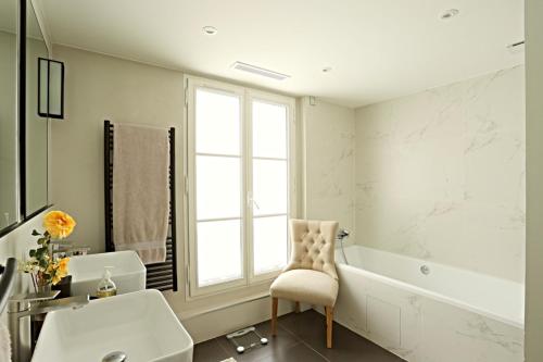 ein Badezimmer mit einem Waschbecken, einer Badewanne und einem Stuhl in der Unterkunft Luxurious Flat Place Vendome in Paris