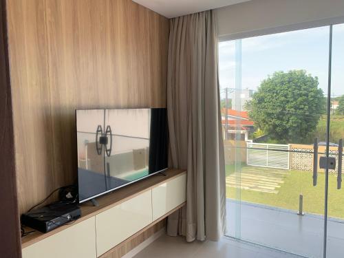 uma sala de estar com televisão e uma grande janela em Casa ilha Itaparica em Armação do Tairu
