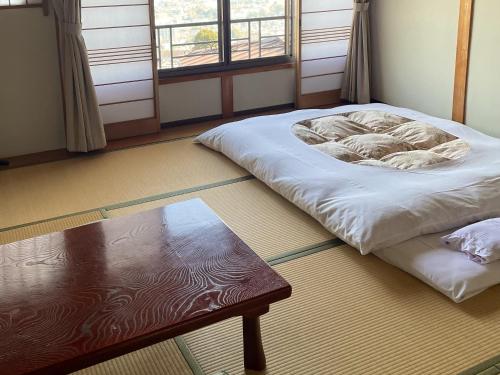 a room with a bed and a table and windows at Kanko Ryokan Yamato in Ikuma